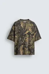Sudadera relaxed fit con estampado de hojas en tonos verde, marrón y negro. Tiene cuello redondo, manga corta y bajo irregular con aberturas laterales.