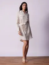 Vestido camisero corto a rayas verticales color beige, con cuello con solapa, abertura central con botones, bolsillos aplicados en el pecho y lazo de ajuste en la cintura.