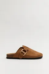 Zuecos color marrón con hebilla metálica dorada lateral y base anatómica de corcho.