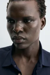 Pantalón chino negro de corte relajado (relaxed fit) con tiro medio, confeccionado en algodón con elasticidad. Presenta bolsillos delanteros y bolsillos traseros de vivo, con cierre frontal de cremallera y botón.