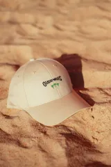 Gorra color crudo con bordado frontal de la frase "Glossy Waves" y dos palmeras.