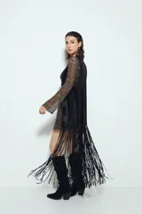 Chaleco largo color beige claro, estilo chaleco de gamuza, con apliques metálicos circulares perforados y largos flecos en el ruedo.