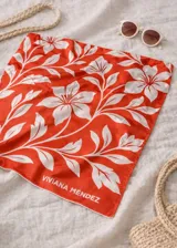 Pañuelo cuadrado de tela ligera, color naranja vibrante, con estampado floral en blanco que simula un diseño botánico o hawaiano. Lleva el nombre "VIVIANA MÉNDEZ" estampado en la esquina inferior.