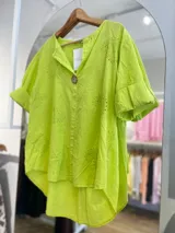 Blusa color crema con cuello camisero, mangas cortas con dobladillo y cierre frontal con un botón de madera. Presenta bordados con motivos de paisley y perforaciones.