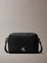 Cartera bandolera Calvin Klein negra de cuero sintético granulado, con correa ajustable, cierre de cremallera y logo metálico "CK" en el frente.