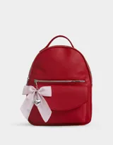 Mochila roja de cuerina con bolsillo frontal con solapa y charm colgante de corazón y moño a rayas.
