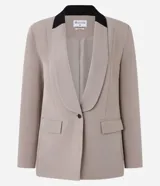Blazer de tejido plano color beige con estructura de sastrería, cuello smoking con contraste negro en la nuca, botón único para cierre y solapas delanteras que simulan bolsillos.