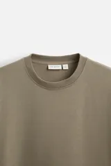 Camiseta color caqui de corte cuadrado, confeccionada en tejido de algodón pesado. Tiene cuello redondo y mangas cortas.