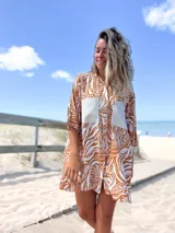 Camisero corto de manga tres cuartos, con cuello camisero y botones frontales. Presenta un estampado botánico en tonos marrón óxido y blanco, con dos bolsillos cuadrados de color beige liso en el pecho.