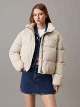 Campera puffer color beige claro con logo de Calvin Klein bordado en el pecho. Tiene cuello alto, cierre con cremallera y botones a presión, bolsillos laterales y puños elásticos.