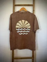 Remera marrón con efecto gastado, corte amplio y estampado en la espalda con un sol naciente sobre el mar.