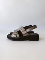 Sandalias de cuero color peltre con plataforma y suela track color negro. Presentan dos tiras anchas con hebillas plateadas y tira trasera ajustable.