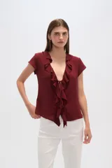 Blusa blanca de viscosa con escote en V, mangas cortas y volados frontales con lazo ajustable.