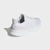 Championes de running Adidas Ultrarun 5, color blanco con detalles en rosado pálido en las tres franjas laterales y el talón. Presentan una suela gruesa y amortiguada.