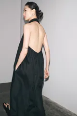 Vestido midi negro de lino, con cuello halter, hombros descubiertos, espalda descubierta, cierre frontal con botones y bajo asimétrico.