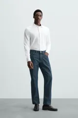 Camisa celeste a rayas verticales blancas, de corte recto, con cuello italiano abierto, mangas largas con puños abotonados y cierre frontal con botones.