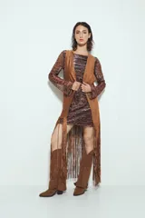 Chaleco largo color beige claro, estilo chaleco de gamuza, con apliques metálicos circulares perforados y largos flecos en el ruedo.