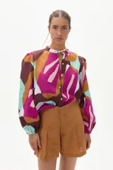 Camisa de lino con estampado abstracto en tonos marrón, fucsia, celeste y blanco. Tiene cuello mao, mangas largas abullonadas y cierre frontal con botones.
