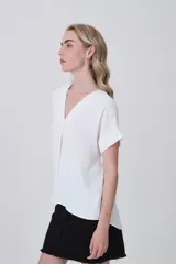 Blusa holgada de poliéster color blanco, con escote en V profundo y pinzas frontales que generan caída. Mangas cortas.