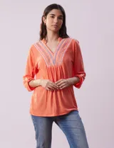 Blusa blanca de poliéster y rayón con escote en V bordado y mangas tres cuartos regulables con presilla y botón.