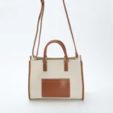 Bolso tipo shopper de lona color beige con detalles en cuero color marrón. Tiene doble asa corta de mano y correa larga regulable y extraíble para usar al hombro.