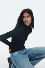 Top ajustado de punto acanalado suave, color negro, con cuello alto y mangas largas acampanadas.