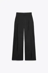 Pantalón negro de tiro alto con trabillas, doble pliegue, bolsillos laterales y tapetas en la espalda. Tiene pernera ancha y cierre frontal con cremallera y gancho metálico.