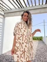 Vestido camisero de lino color beige con estampado abstracto en marrón. Tiene cuello camisero, cierre frontal con botones y mangas 3/4 con trabillas.