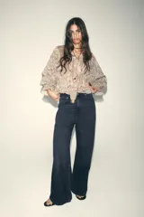 Camisa estampada con motivos paisley en tonos beige, rosa, lila y amarillo. Tiene cuello redondo con lazos, mangas largas abullonadas con puños elásticos y volantes en el delantero.