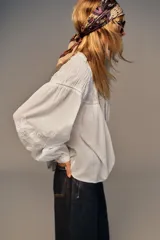 Camisa blanca de cuello redondo con detalle de nido de abeja y entredoses. Manga larga con bordados a tono y cierre trasero con botones.