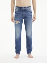 Jeans de denim azul con rotos, de corte slim tapered, talle medio, cinco bolsillos y cierre con cremallera.
