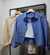 Camisa celeste con rayas verticales blancas, de manga larga con puños abotonados y corte holgado.