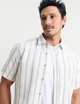 Camisa de manga corta a rayas verticales celestes y blancas, con cuello clásico y botones marrones.