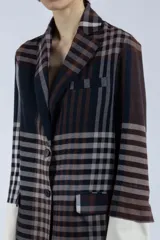 Blazer con estampado a cuadros en tonos marrones y negros, de corte recto y silueta relajada. Presenta solapas clásicas, cierre frontal con botones y bolsillos con tapa. Mangas largas con puños blancos.