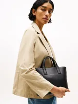 Cartera tote negra con textura granulada, doble asa corta y correa larga de tela con logo de la marca en blanco y negro.