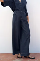 Pantalón de jean azul oscuro, corte wide leg, tiro alto con pinzas delanteras, bolsillos laterales y cierre frontal con cremallera y botón.