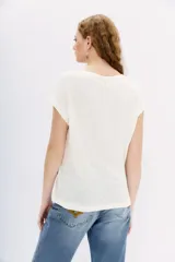 Remera de lino color crudo con cuello en V y mangas cortas. Tiene tachas plateadas termofijadas en el frente.