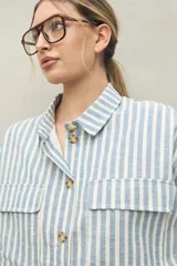 Chaqueta a rayas verticales celestes y blancas, con cuello camisero, cierre frontal con botones, dos bolsillos de parche en el pecho y mangas largas con puños abotonados.