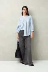 Camisa celeste a rayas verticales, de corte amplio y mangas 3/4. Presenta cuello mao, cierre frontal con botones irregulares y detalle de pespuntes y pinzas en el canesú.