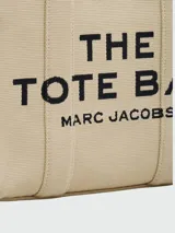 Bolso tote de tela color beige con estampado del logo de la marca en negro. Tiene doble asa de mano y correa de hombro extraíble y ajustable en color negro.