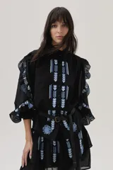 Blusa blanca de viscosa con cuello mao, cierre frontal con botones, mangas largas abullonadas con volados y bordados florales.