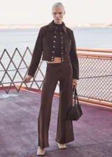 Chaqueta corta marrón de gamuza con cuello camisero, cierre frontal con botones a presión, dos bolsillos de parche con solapa en el pecho y puños abotonados.