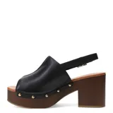 Sandalia de mujer con capellada de cuero negro, diseño cerrado en la punta (peep-toe) y pulsera ajustable con hebilla dorada en el tobillo. Posee una plataforma y taco alto de madera oscura, con detalles de tachas metálicas doradas en la unión entre la capellada y la plataforma.