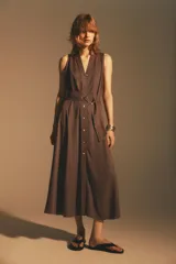 Vestido midi marrón sin mangas, con cuello solapa, escote en pico, cierre frontal con botones y cinturón de la misma tela con hebilla metálica.