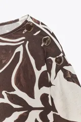 Blusa de cuello redondo y manga larga ancha con botones en los hombros. Estampado floral en tonos marrón y blanco.