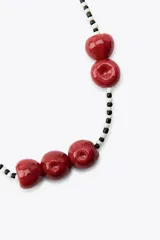 Collar corto con cuentas pequeñas blancas y negras, y dijes grandes de cerezas rojas. Cierre de mosquetón dorado.