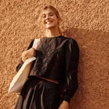 Blusa corta negra con bordado floral, mangas largas abullonadas y cuello redondo.