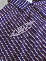 Camisa de manga corta con corte híbrido boxy fit/oversize, confeccionada en algodón. Disponible en tres diseños: a cuadros marrones, a rayas blancas y negras, y a rayas burdeos y blancas. Presenta bordados de diseño propio de la marca.