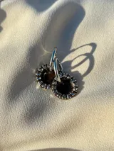 Par de aros colgantes con argolla de acero quirúrgico, dije circular de resina negra y borde de strass plateado.