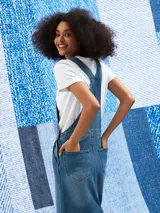 Jumper largo de denim azul con breteles regulables, bolsillos frontales y corte recto.